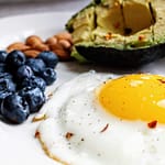 A nutritious breakfast featuring a fried egg, avocado, blueberries, and almonds.