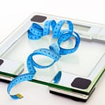 A digital glass weighing scale with a blue measuring tape, symbolizing weight management.